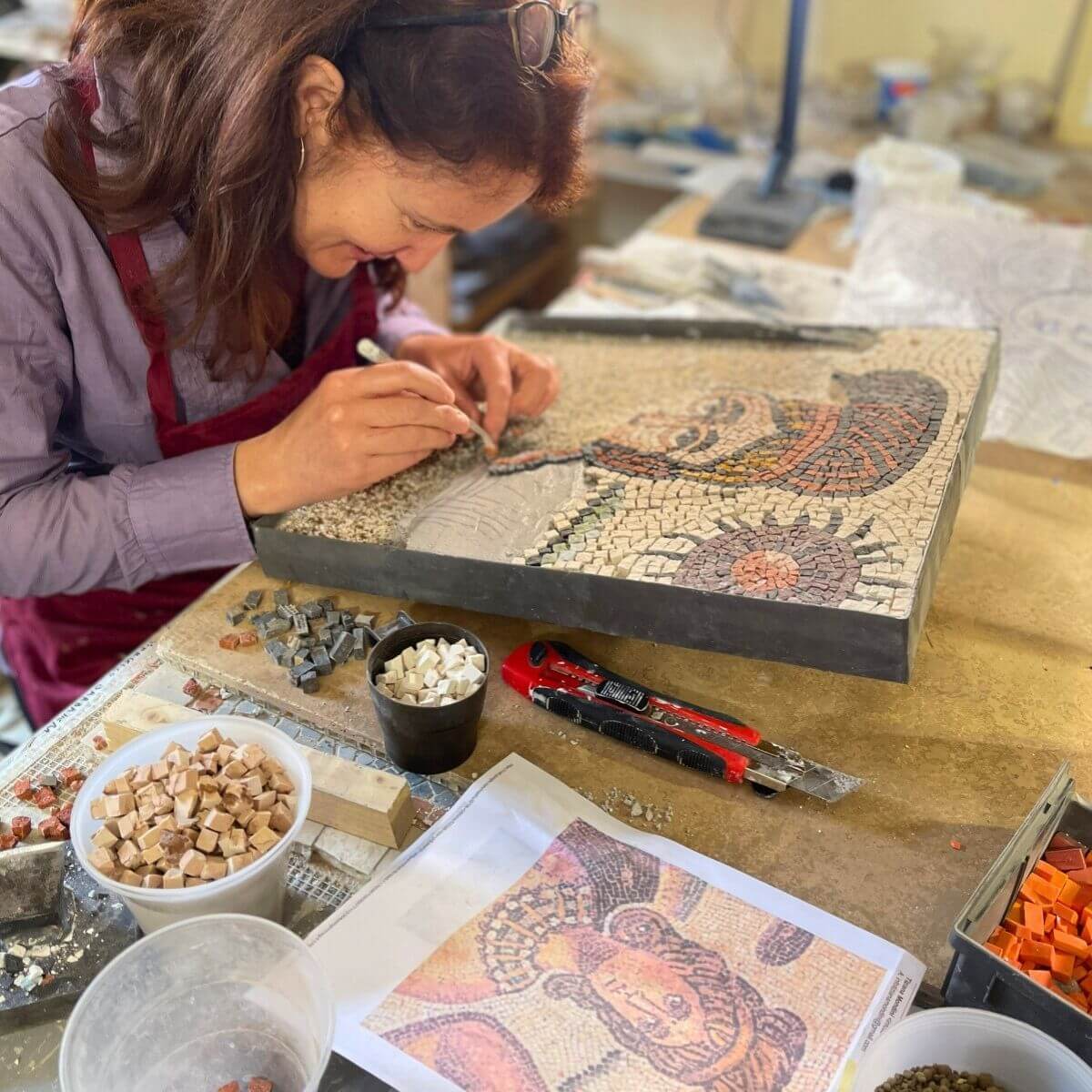 Studentessa mentre lavora alla costruzione di un mosaico effettuato con la tecnica del micromosaico romano. La studentessa sta posizionando alcune micro tessere sulla malta.
