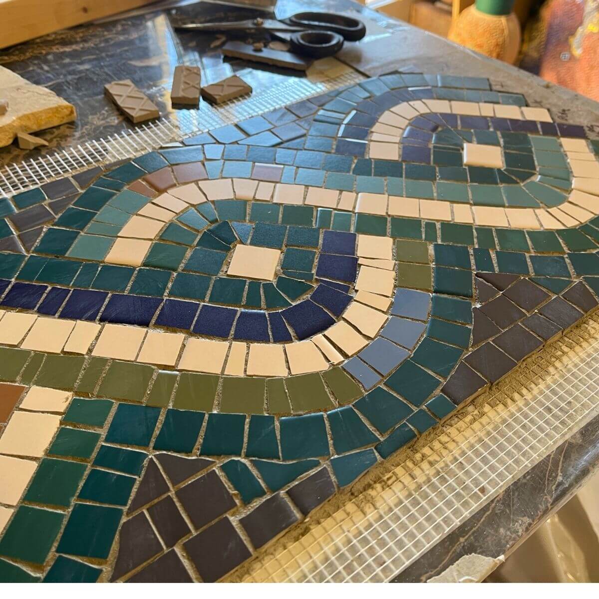 Realizzazione di un mosaico geometrico con tessere colorate durante il corso di mosaico alla scuola In Tessere.
