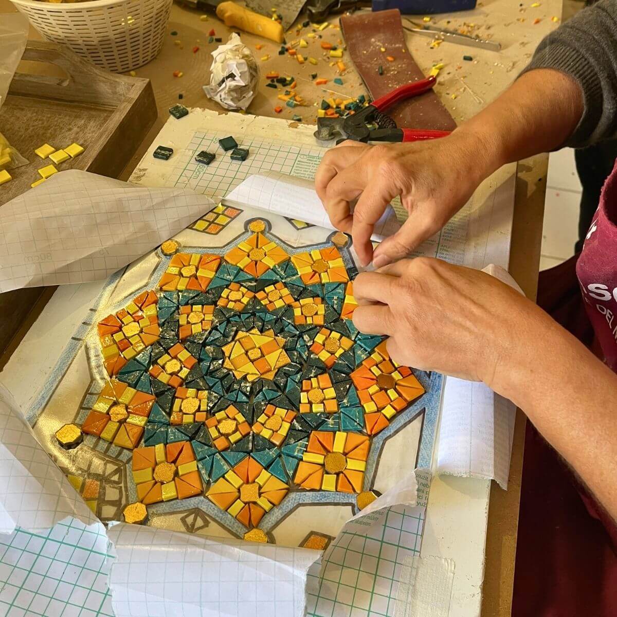 Allieva realizza un motivo floreale in mosaico con tessere dorate durante la lezione pratica.