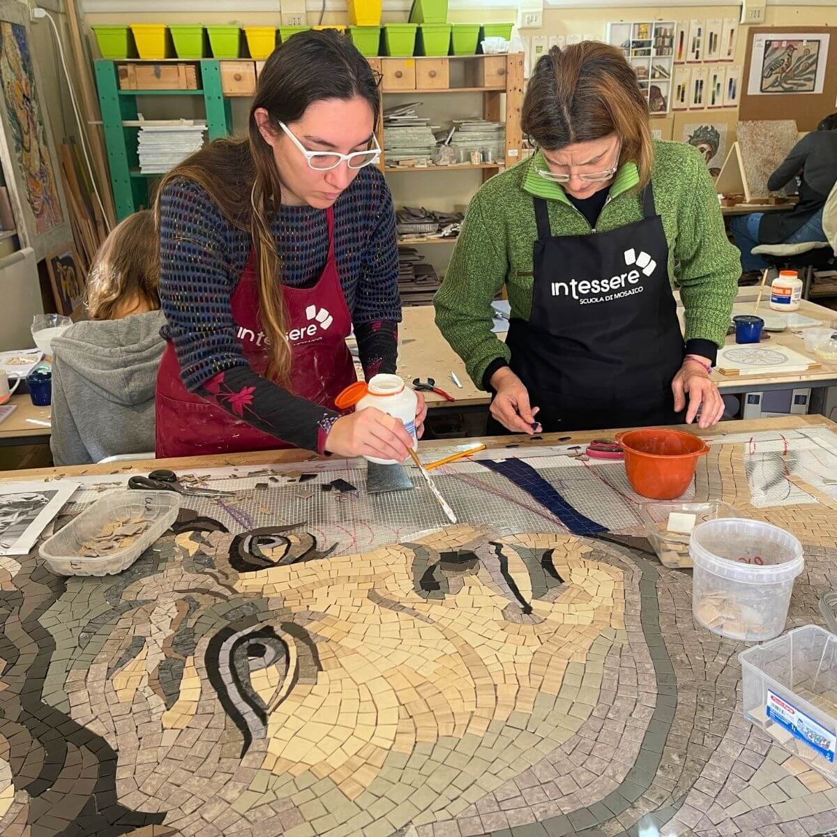 Partecipanti al corso di mosaico industriale lavorano insieme su una grande composizione con linoleum