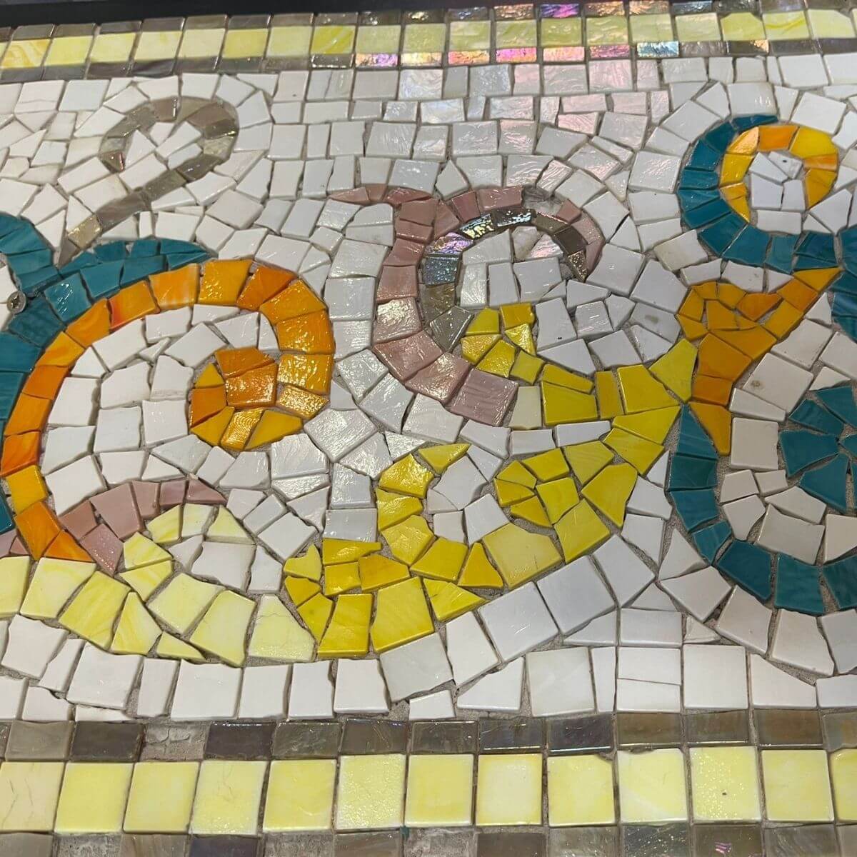 Motivo ornamentale in mosaico industriale con tessere gialle e bianche, in fase di rifinitura.