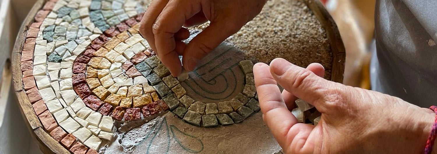 A hand placing some marble tiles and tesserae during the construction of a mosaic kit for adults