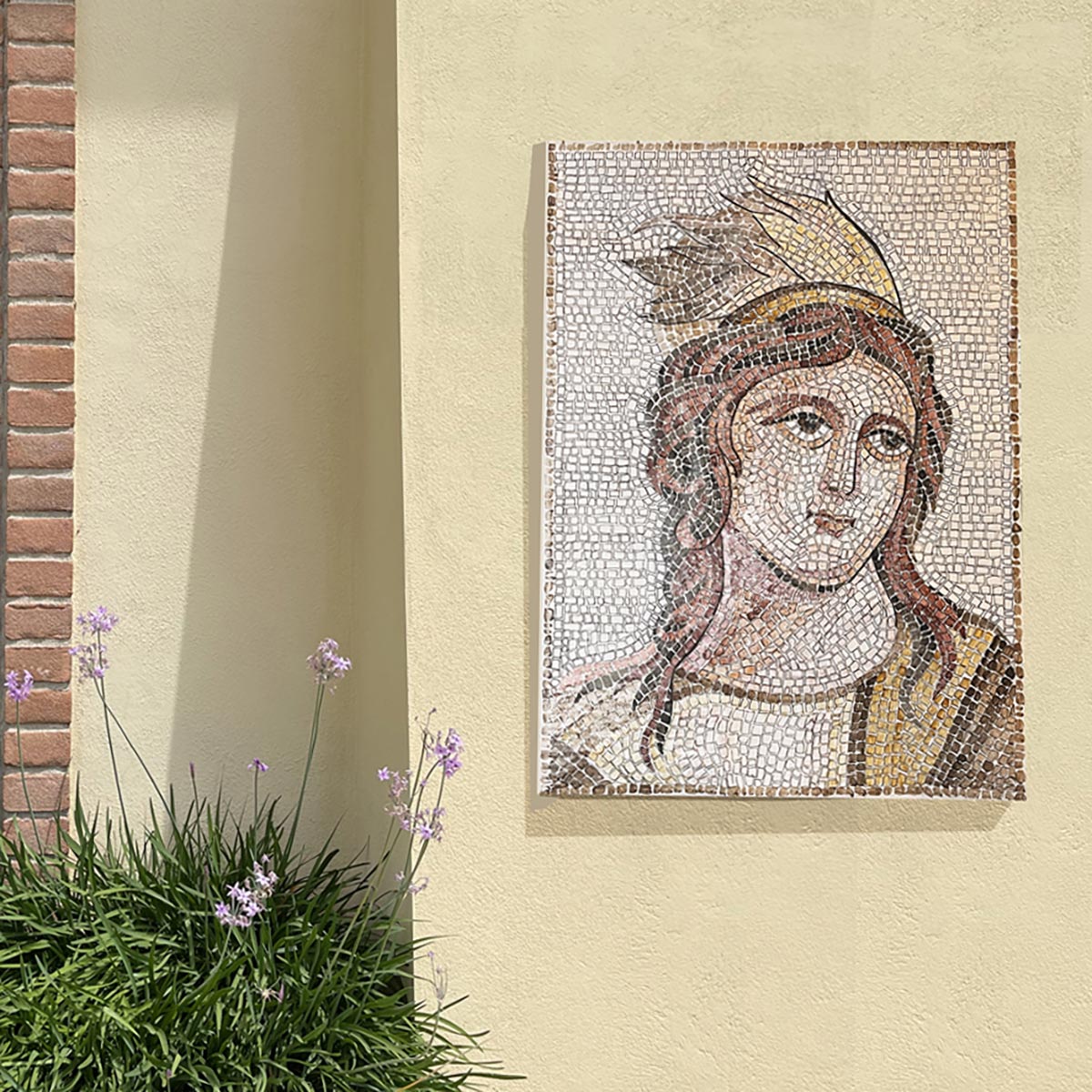 Mosaico raffigurante la figura mitologica Calliope attaccato ad un muro giallo